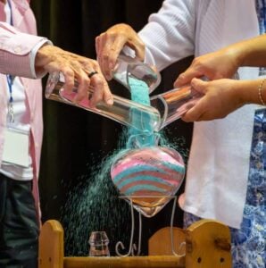 Three sisters pouring different color sand into a heart shaped vase.