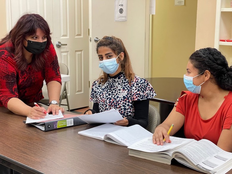 Three students wearing masks while studying together at the DeNeuville Learning Center for Women